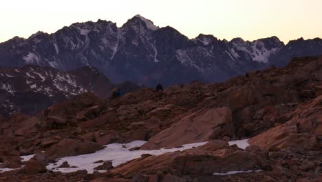 Panning-shot-of-hiker-walking-between-snowy-rocks-on-mountain-landscape-at-Mueller-Hut-Route-after-sunset,NZ