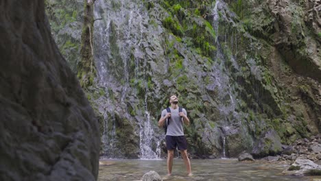 barefoot teenager looking around in front of waterfall.