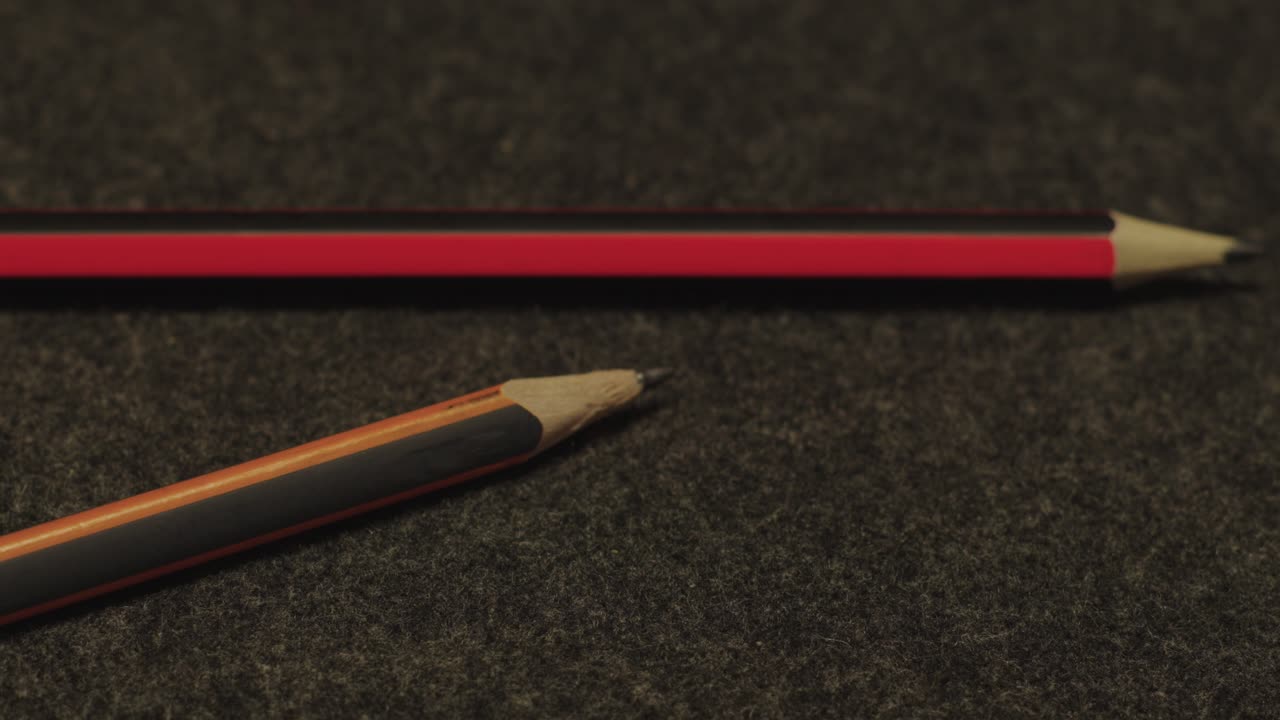 Detailed View Of Two Pencils Red And Orange On Dark Fabric Background