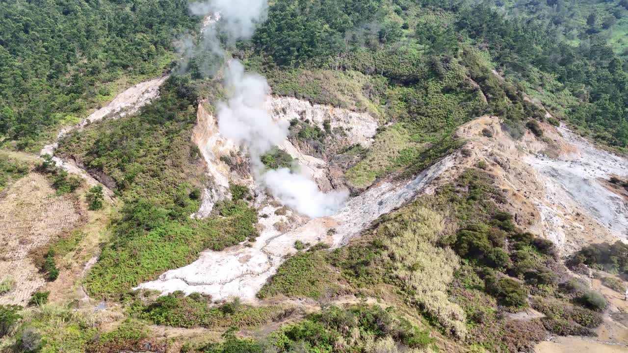 Aerial view of a steaming sulfur crater surrounded by lush green hills and volcanic terrain