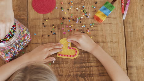 close up top shot of the hands of a little girl and her mother playing with colored beads