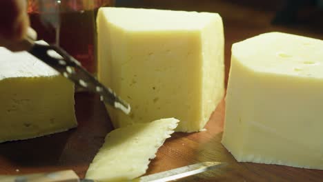 hard cheese on cutting board is sliced near glass of amber alcohol