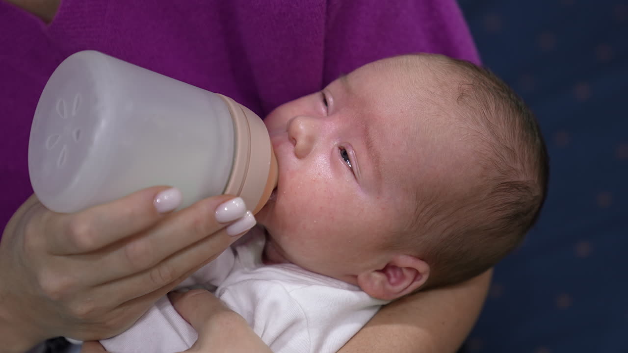 Toddler eating milk from bottle and closing sleepy eyes. Baby gradually falling asleep while eating. Close up.