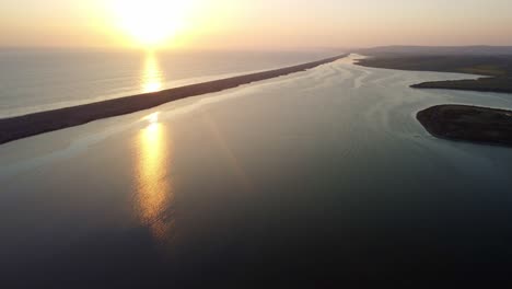 aerial footage pans up to reveal the sun setting over the ocean with portland boundary stones, the. historic landmark across the frame stretching into the distance.