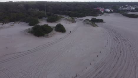 Vista-Aérea-De-Una-Persona-Conduciendo-Una-Moto-En-La-Arena-De-La-Playa-En-Un-Fondo-Natural-Forestal-En-Mar-De-Las-Pampas,-Sudamérica