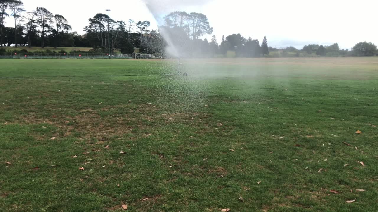 Sprinkler irrigation facilities in the field. Sprinkler spraying water over green grass with rainbow effect. Irrigation system at park. Slow motion