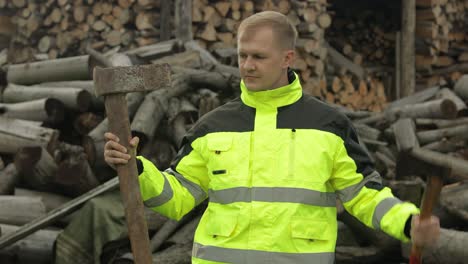 Lumberjack-in-reflective-jacket.-Man-woodcutter-holds-small-and-big-axes-on-his-hands.-Firewood