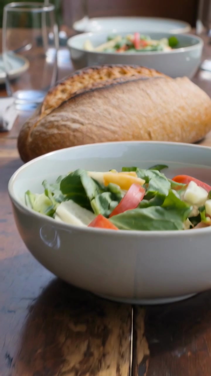 Vertical video: Pulling camera back showing crusty loaf on wood table salads glasses plates at home