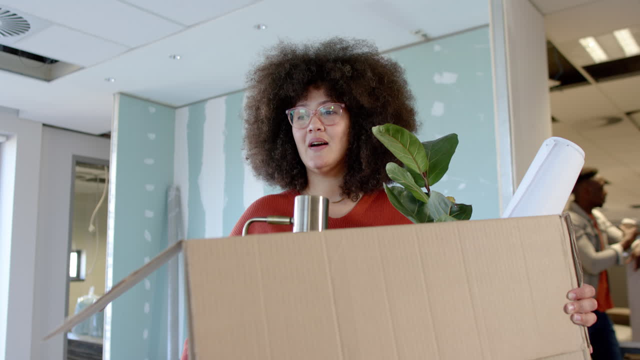 Casual biracial businesswoman carrying box moving into office, slow motion with copy space