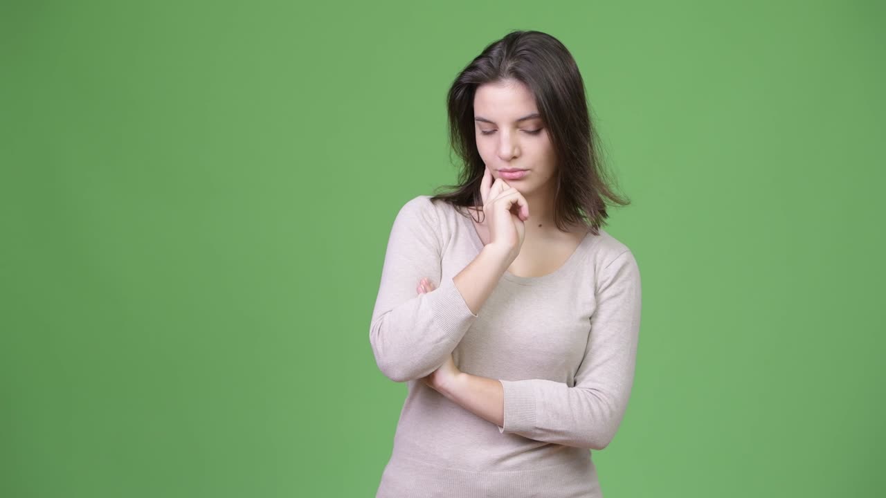 joven hermosa pensando mientras mira hacia abajo contra el fondo verde