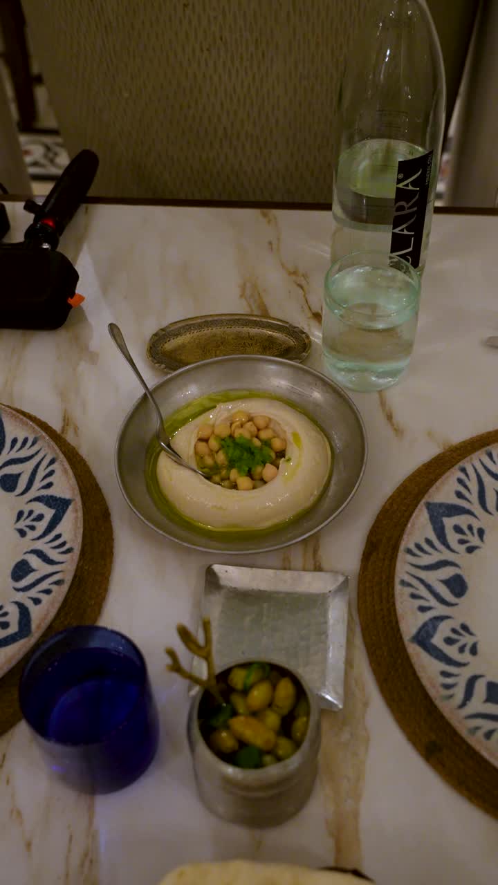 Vertical upward pan across a mezze table in Jordan with taboon flatbread, hummus topped with chickpea and olive oil, plus olive and side dishes—ideal for food and travel use