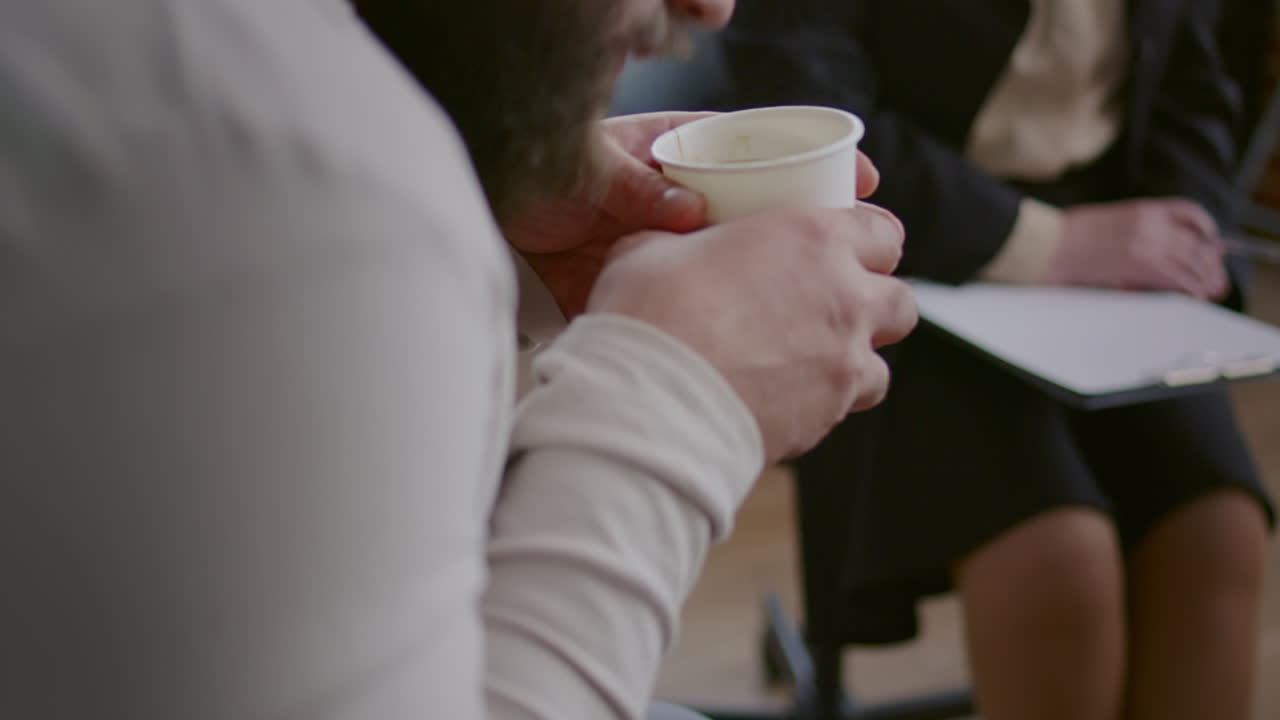 Close up of man drinking cup of coffee and shaking at aa group therapy session
