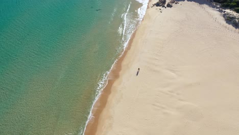 toma aérea hacia atrás de agua turquesa clara en la playa de su giudeu con una pareja de pie en la arena en el sur de cerdeña, italia
