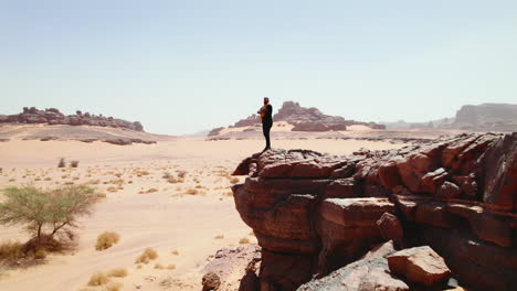 hombre de pie en el borde de una roca mirando el vasto paisaje del desierto en djanet, argelia