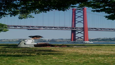 woman reading a book in a park by the dom luís i bridge in lisbon, portugal