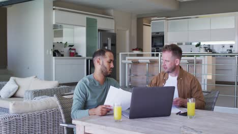 multi ethnic gay male couple sitting at table at homw using laptop