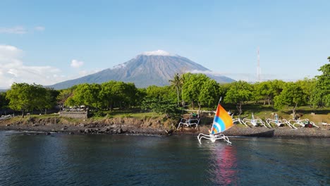 巴厘島傳統漁船的彩色帆船 航行向沿海海灘,被高耸的火山阿貢 (mount agung) 遮蔽.