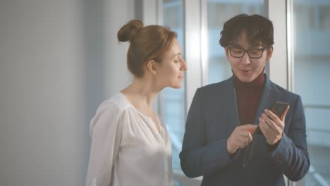 아시아인 사업가 가 백인 여성 동료 에게 스마트폰 에 보고 를 보여 주고 있다