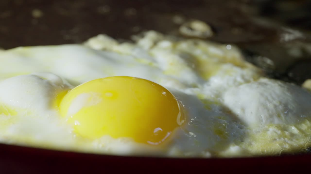 Fish slice lifting fried egg to prevent burning on hot frying pan, macro closeup