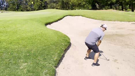 golfer attempts a bunker shot on sunny day