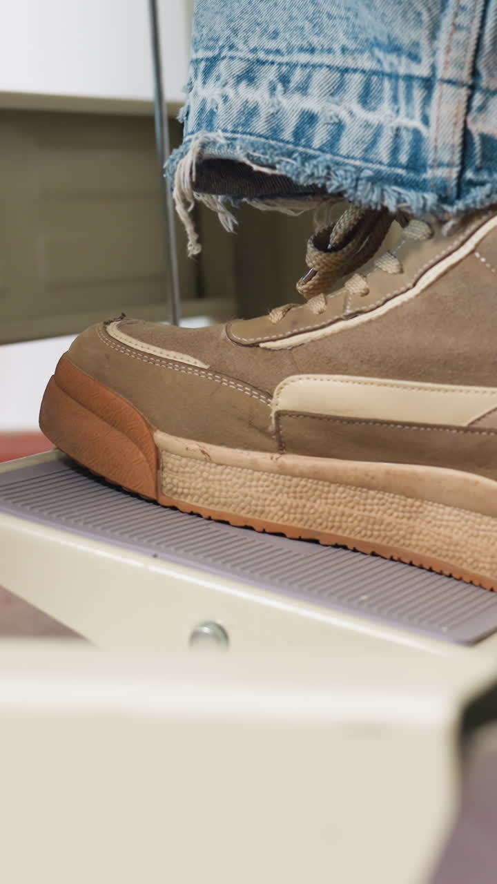 장비 테스트 중 센서 플랫폼 위에 올려진 커프 데님 바지, 텍스처 패드와 접촉하는 스웨이드 신발, 측정 볼트 및 벤치가 배경에 있으며 정밀한 조명이 있는 집중된 실험실 분위기