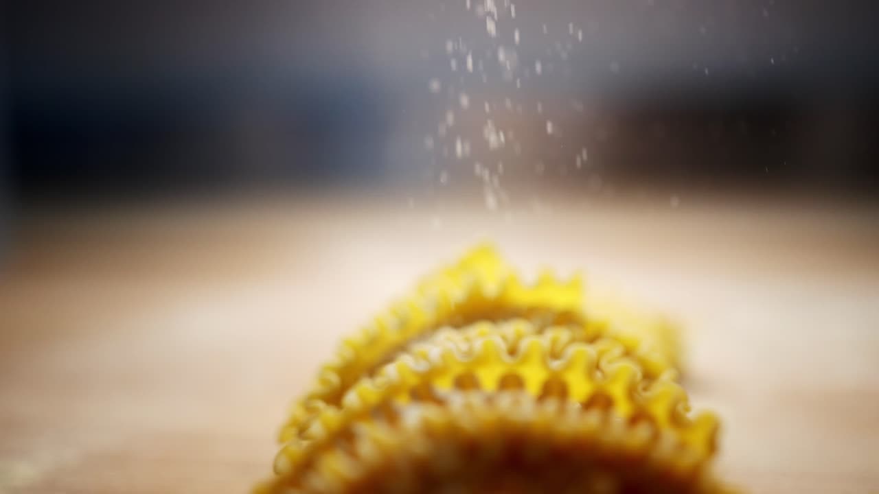 Slow motion view of an unique perspective of semolina particles and flour falling over yellow homemade pasta