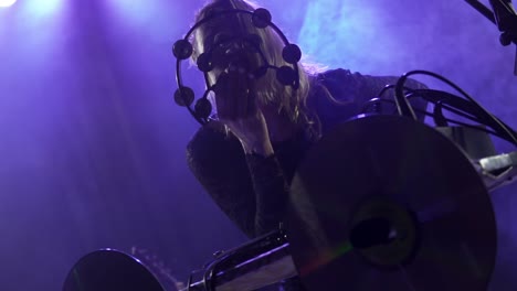 Close-up-portrait-of-the-Caucasian-blonde-singer-performing-on-stage-in-nightclub-lights-with-her-face-behind-the-half-moon-tambourine