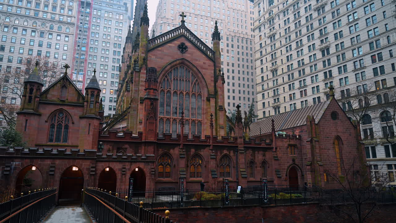 New York, Yhdysvallat, 2. joulukuuta 2025: Trinity Churchin historiallinen goottilainen arkkitehtuuri New Yorkissa. Ulkokuva tummanpunaisesta hiekkakivestä rakennetusta goottilaisesta kirkosta modernien korkeiden toimistorakennusten ympäröimänä.
