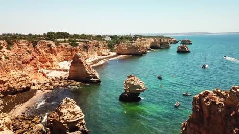 ponta da piedade in lagos, algarve region of portugal, shows turquoise waters, rock formations, cliffs, boats, and sunny weather during summer, establishing drone shot