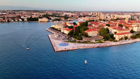 stunning aerial drone view circling zadar’s old town at sunset, capturing the sea organ, greetings to the sun installation, deep blue adriatic, and golden-hour reflections.