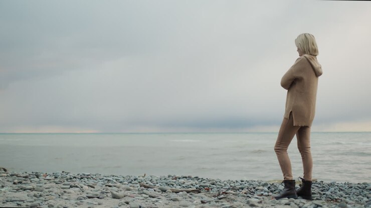 A woman in a warm knitted sweater looks at the sea where the storm begins
