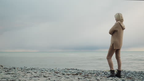 a woman in a warm knitted sweater looks at the sea where the storm begins