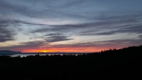 Tiro-De-Dron-Ascendente-De-La-Puesta-De-Sol-Sobre-El-Agua-Y-El-Bosque-Del-Noroeste-Del-Pacífico