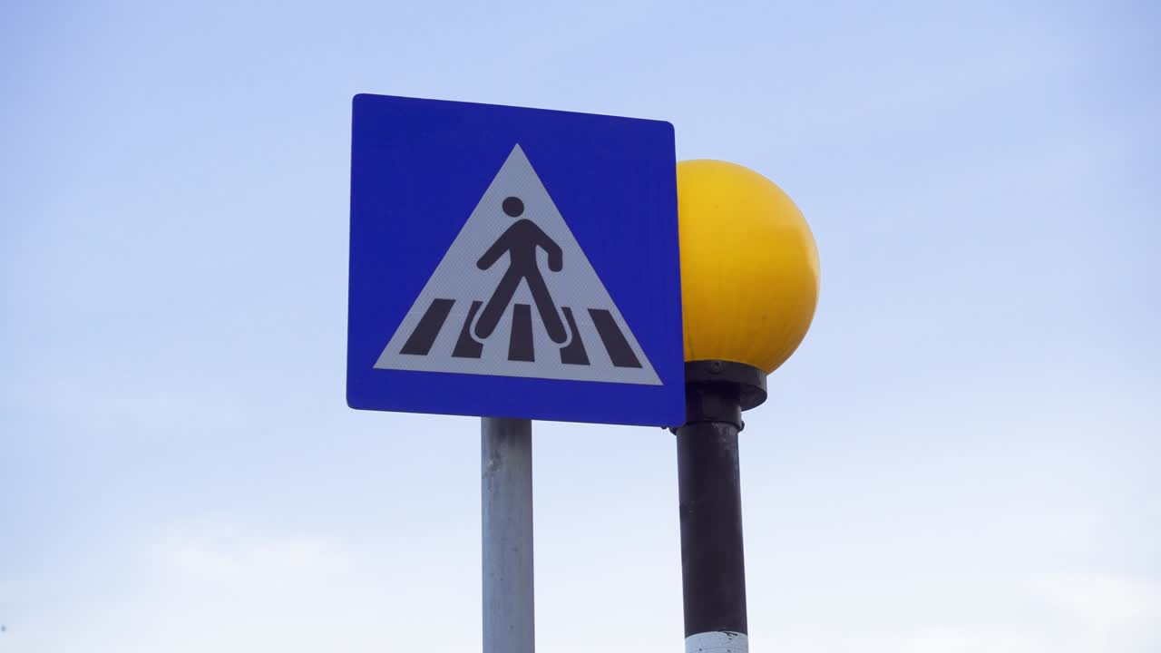 Unregulated pedestrian crossing sign against blue sunset sky. Yellow round traffic light flashing