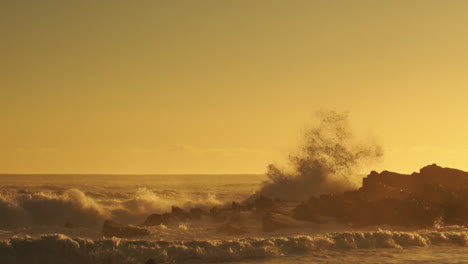 Olas-Del-Mar-Agitadas-Rompiendo-En-Las-Rocas-Creando-Un-Enorme-Rocío-Durante-La-Puesta-De-Sol-Dorada---Toma-Panorámica-Amplia