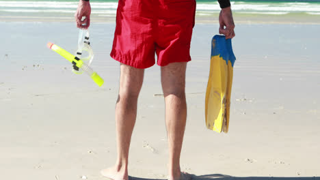 hombre mayor con aletas y máscara de buceo de pie en la playa