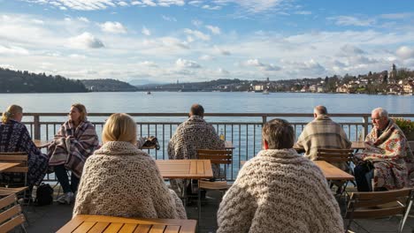 cozy gatherings by the lake: a relaxing scene of people wrapped in warm blankets, enjoying scenic views and serene waters under a bright sky