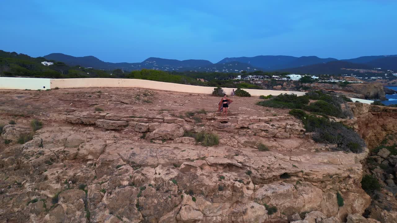 dancing Woman expressing freedom and movement by the sea at a beautiful travel destination Cala Llentia Ibiza. Amazing aerial view flight panorama orbit drone