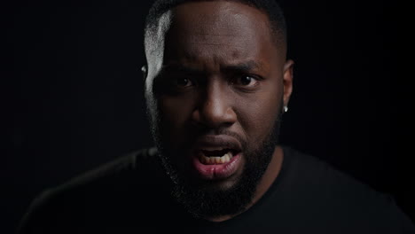 wicked afro guy screaming on black background. closeup man yelling in studio