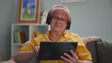 elderly woman with headphones works remotely on a tablet