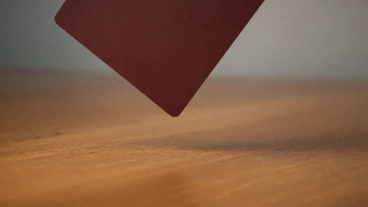 Releasing dark matte card with rounded corners, descending onto wooden tabletop, casting shadow