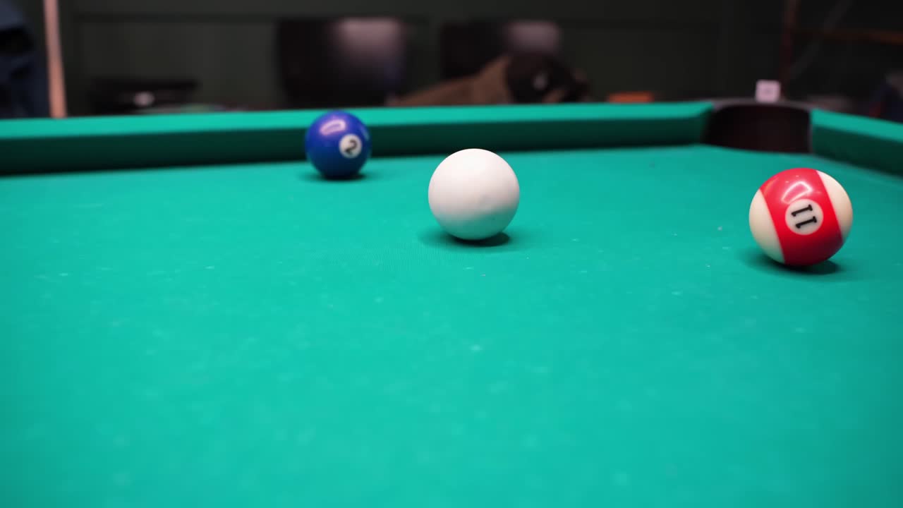 Close-up van een biljarttafelscène met speelbal, blauwe 2 en rood gestreepte 11 nabij een hoekzak op groen laken, met geringe scherptediepte in een bar-lounge.