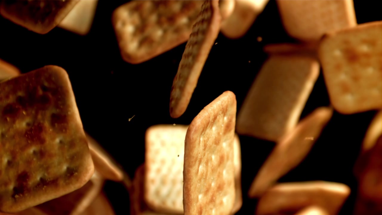 Cracker dorati e croccanti che cadono al rallentatore su uno sfondo nero.