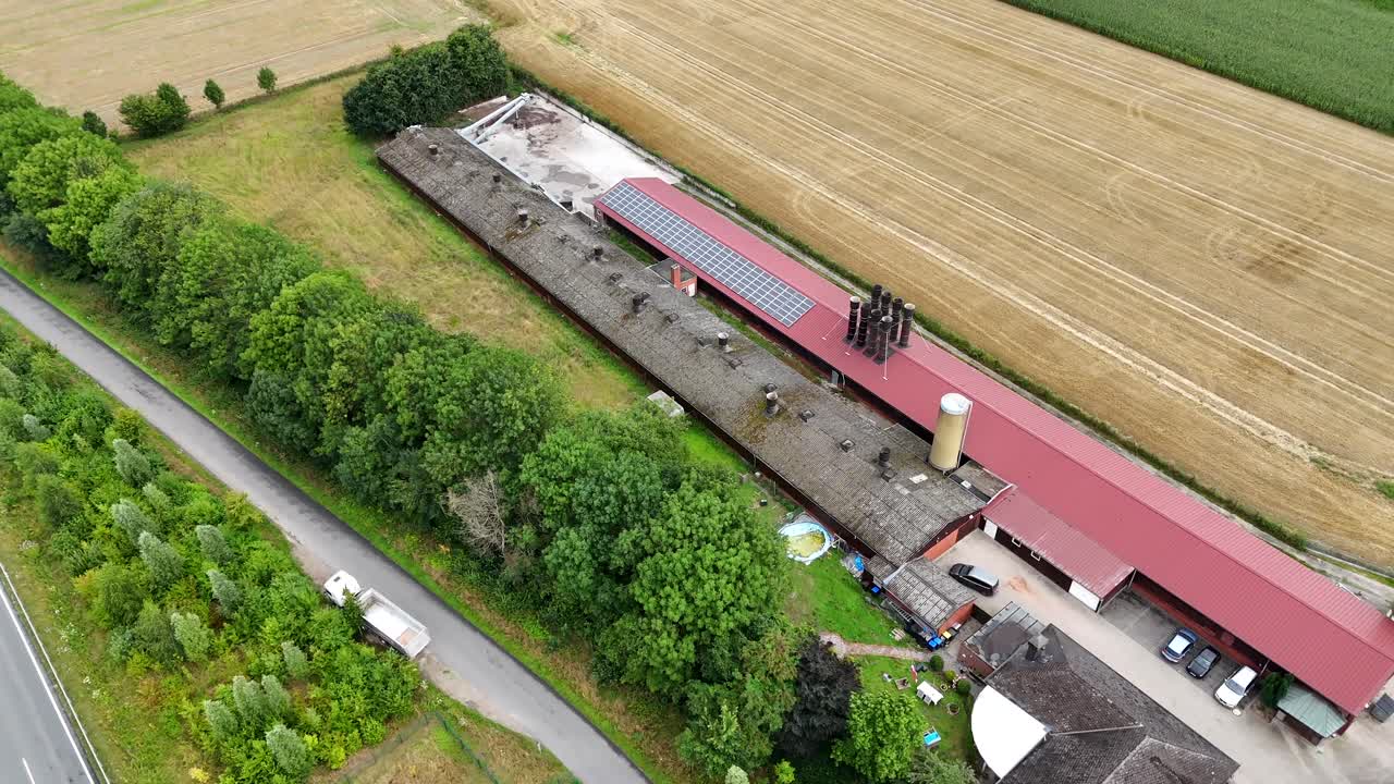 Red barn building with solar panels on American farmstead. Driving cars on suburb intersection road on summer. Aerial top down shot. Quiet and idyllic rural landscape scene