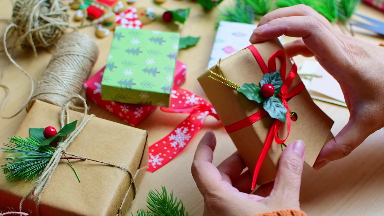 Mani di donna che decorano un regalo di Natale con agrifoglio.