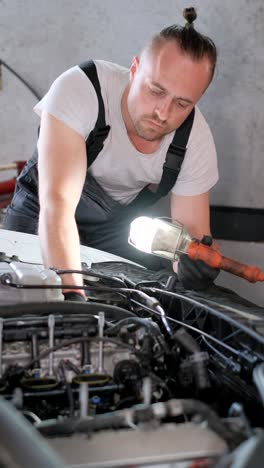 mechanic inspecting a car engine with a flashlight