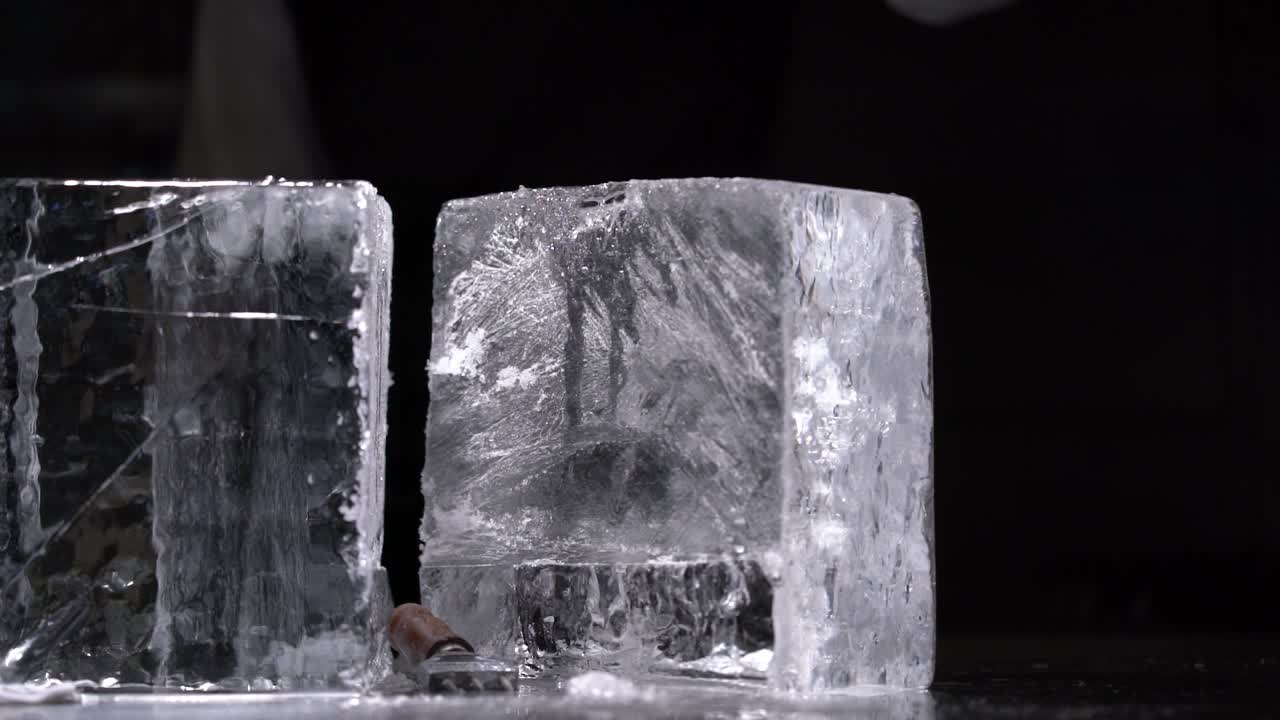 The bartender is hitting the top of the ice pick with a hammer to make the big crystal clear ice block separate from each other.