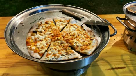 pizza en pedazos o rebanadas en una bandeja de metal sobre un fondo de mesa de madera, con una fina corteza de pastel, primer plano. 4k
