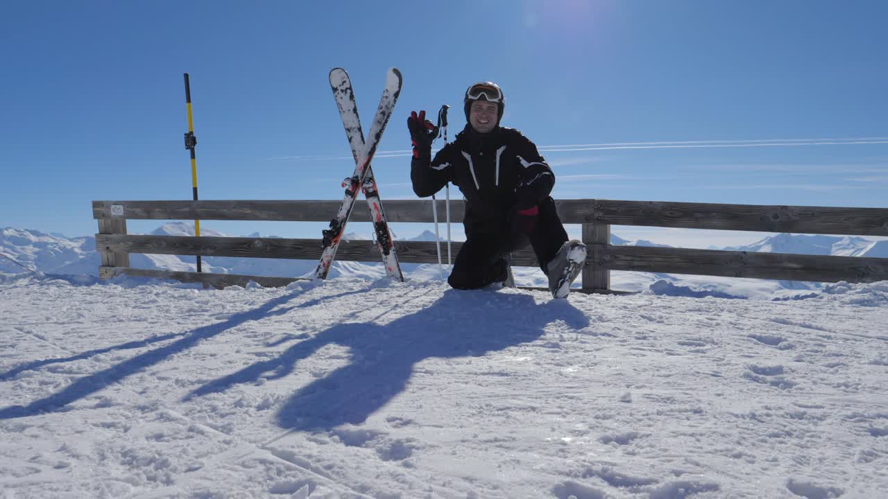 산에서 웃는 행복한 스키 선수는 은 몸짓을 보여주고 엄지손가락을 올리고 팔을 들어 올립니다.