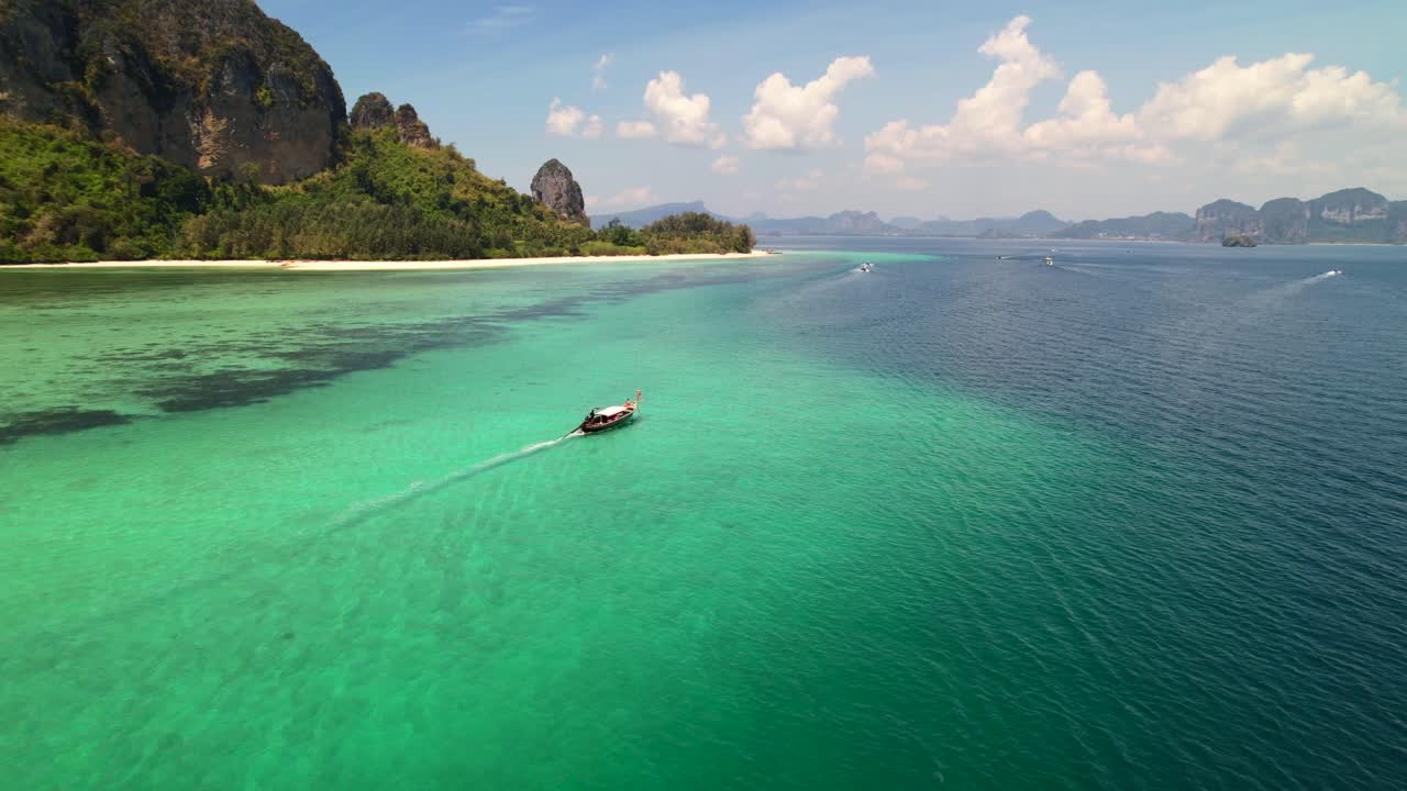 Ampia veduta aerea di una barca longtail thailandese che naviga nel mare turchese delle Andamane, circondata da barriere coralline e grandi montagne calcaree dell'isola di Ko Poda a Krabi, Thailandia, in una soleggiata giornata estiva